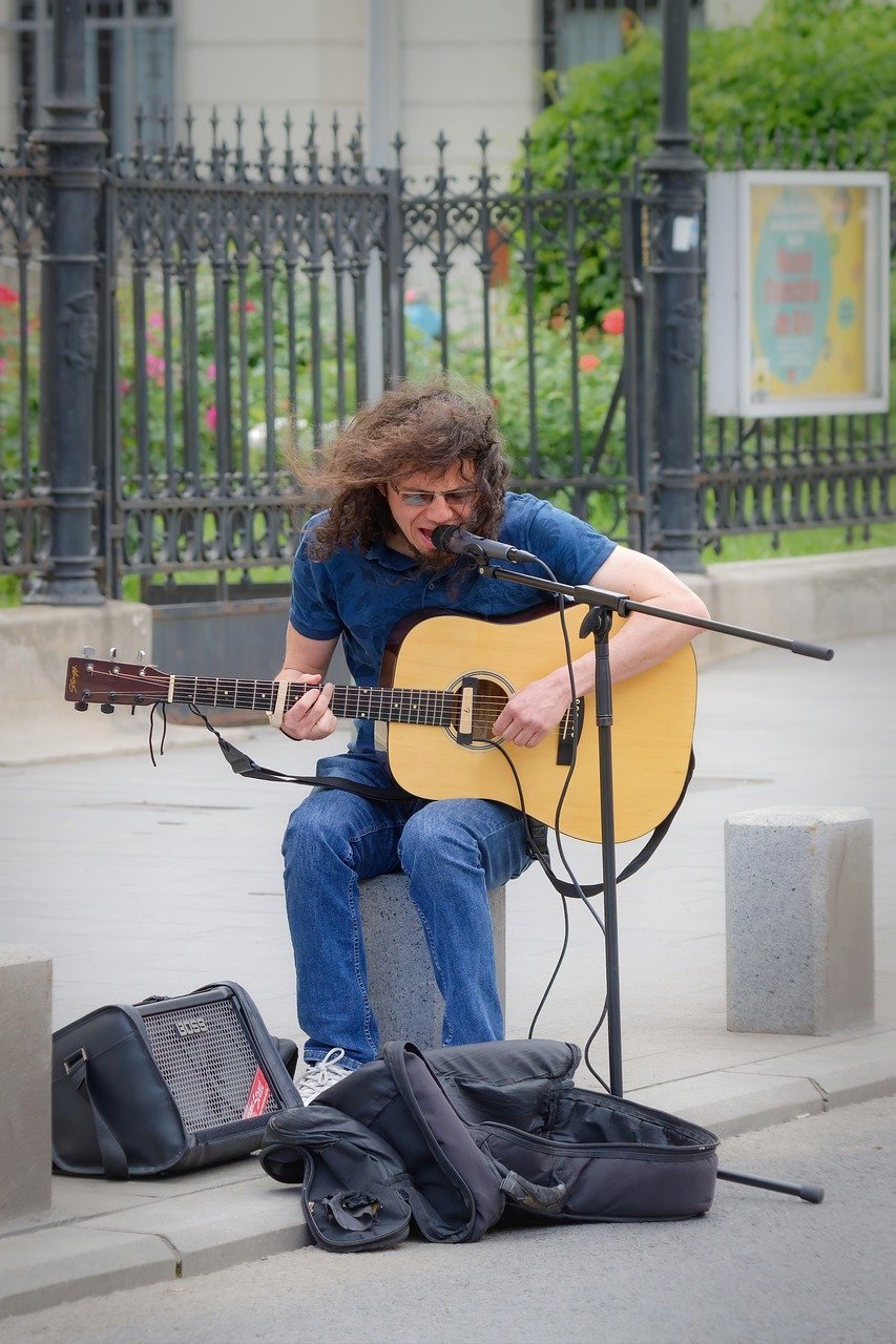 man, young, busker, playing, guitar, voice, microphone, sitting, stone, sidewalk, street, urban, lifestyle, snapshot