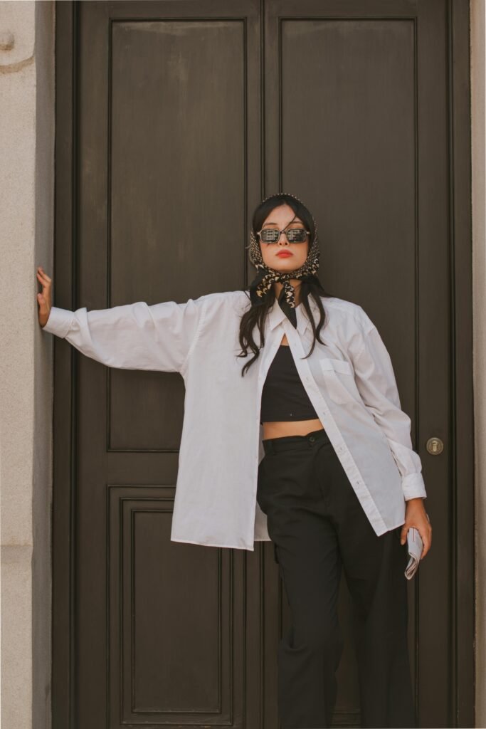 Stylish woman in a headscarf and sunglasses poses against a classic wooden door, exuding elegance.