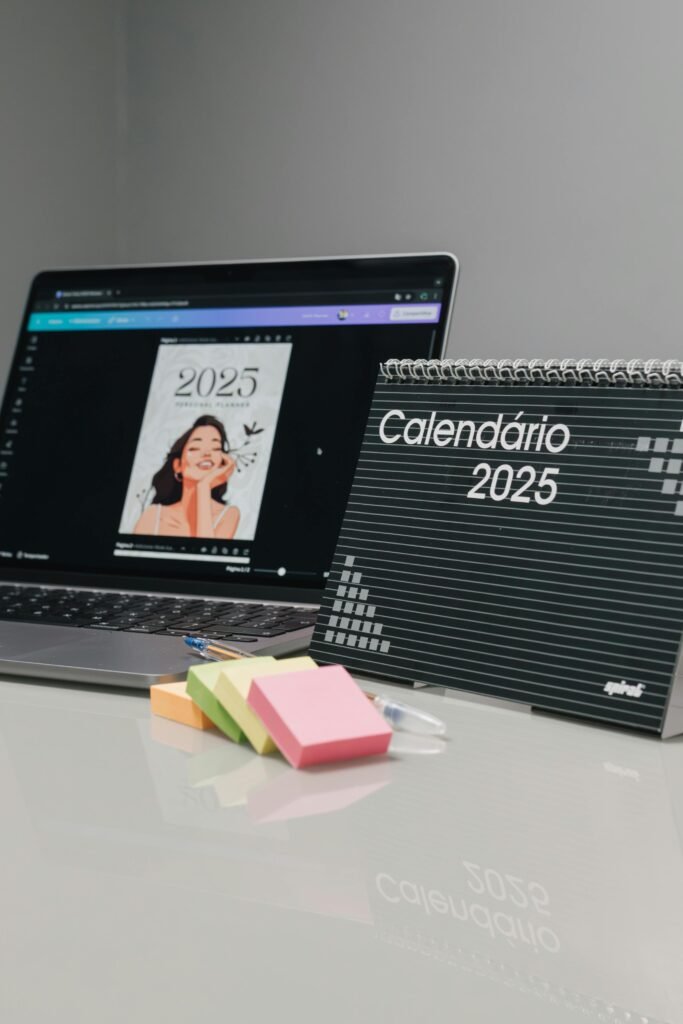 Spiral-bound 2025 desktop calendar beside a laptop and colorful sticky notes.