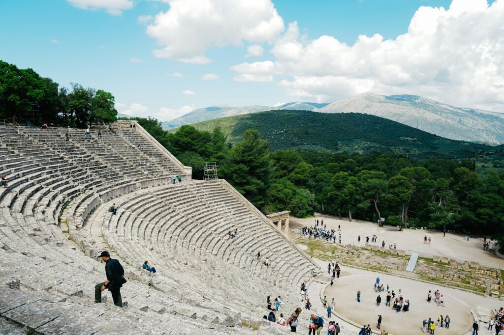 View of the historic Greek amphitheater with people exploring, set against a scenic mountain backdrop.