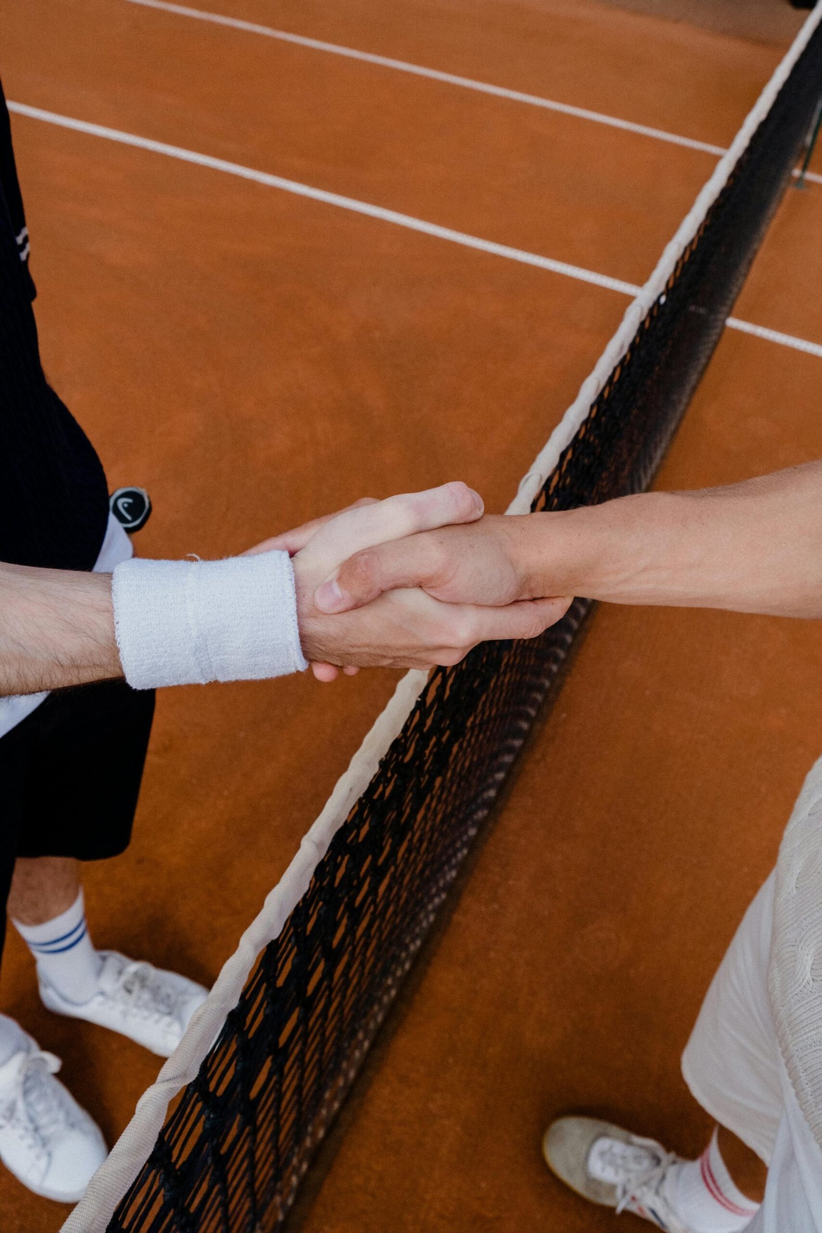 Two tennis players in a friendly handshake over a clay tennis court net, symbolizing sportsmanship.