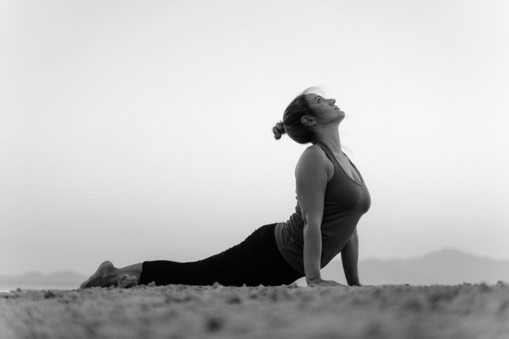 Black and white photo of a woman doing yoga's upward facing dog pose on a beach.